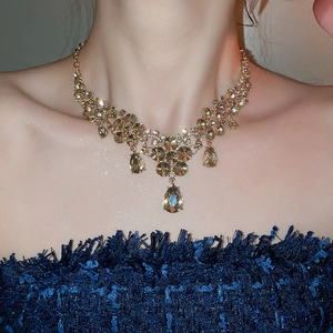 Close-up of luxury gold-tone waterdrop pendant necklace set on a model in a blue dress