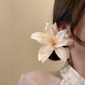 Detail of a champagne fabric lily hair clip worn on a bun with matching pearl earrings