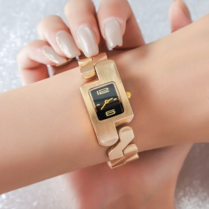 Detail of champagne gold geometric bangle watch with a black dial on woman's wrist