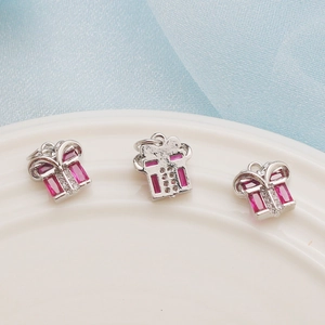Macro view of gift box shaped silver charms with pink gemstones on a white plate
