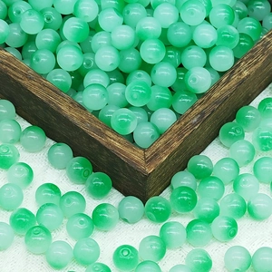 Detail of 10mm green gradient glass beads with natural texture in a dark wooden tray