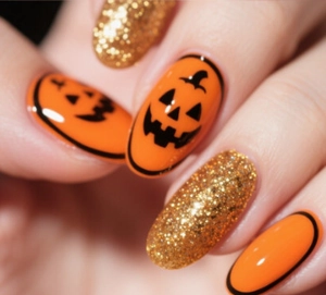 Detail of short oval press-on nails featuring orange pumpkin faces and gold glitter finish