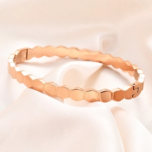 Close-up of rose gold hexagonal honeycomb bangle with brushed metal texture on silk background