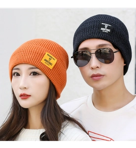 Close-up of knit beanies in orange and dark grey showing detailed texture and patch