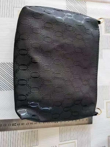 Macro view of black embossed clutch bag with chain pattern and size reference ruler