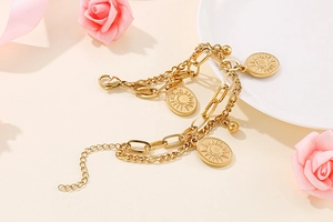 Detailed view of layered gold chain bracelet featuring sun pattern oval charms on a white plate