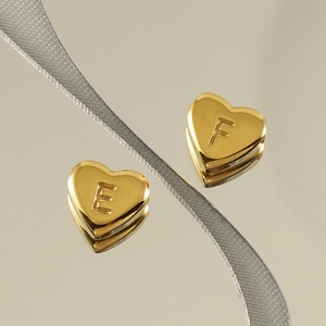 Macro shot of 18K gold heart charms with engraved letters E and F on reflective surface