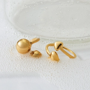 Minimalist gold hollow heart and spherical ring set displayed on clean textured background