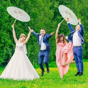 White paper parasols held by guests jumping during a lively outdoor lawn wedding party