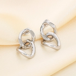 Macro shot of silver interlocking oval link earrings on smooth yellow silk fabric
