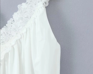 Dettaglio dell'elegante pizzo bianco e dello scollo a V profondo sull'abito senza maniche