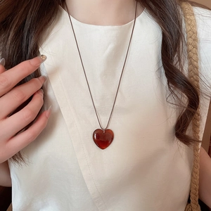 Dettaglio ravvicinato di un ciondolo a cuore in resina rossa su un cordino intrecciato