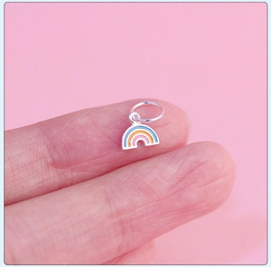 Macro shot of a tiny colorful rainbow enamel pendant on a fingertip for size comparison