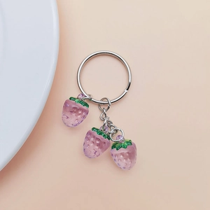 Detail of silver metal keychain with three purple resin strawberries on pink background
