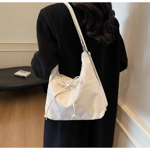 Detail of cream white bow hobo bag with slim strap shown on model over black coat