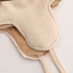 Nahaufnahme der beigen Strickmütze mit dickem Plüschfutter und geflochtenen Bindebändern
