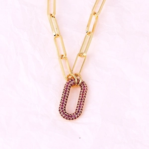 Macro detail of a gold-plated link necklace with a purple rhinestone oval pendant