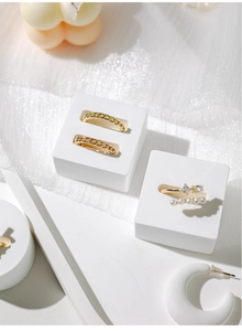 Close-up of gold chain rings and pearl jewelry displayed on white geometric stands
