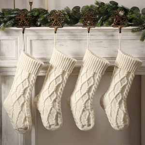 Set of four cream knitted Christmas stockings with diamond pattern hanging on a white fireplace