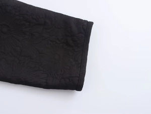 Close-up of black floral embroidery and textured jacquard fabric on a jacket