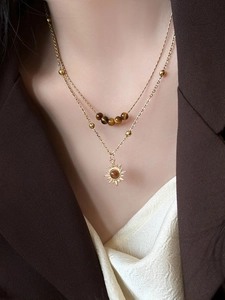 Macro detail of a gold double-layer necklace with tiger eye beads and sun pendant
