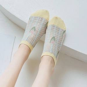 Socquettes en résille jaune pâle avec broderie tulipe rose présentées sur pied en studio