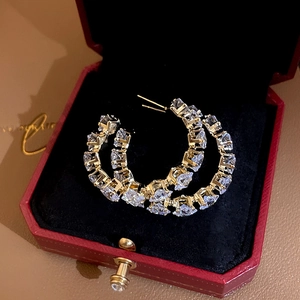 Detail of gold C-shaped hoop earrings with square zircons inside a red jewelry box
