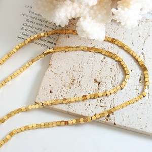 Minimalist gold square bead necklace displayed on a beige stone and coral background
