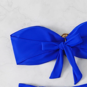 Detail of royal blue bandeau bikini top with tortoiseshell ring and bow on marble