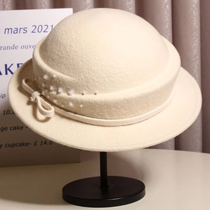 Detailed view of elegant wool felt bucket hat with bow and pearls on a display stand