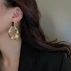 Detailed view of a gold-toned crinkled metal earring featuring a dark rectangular gemstone