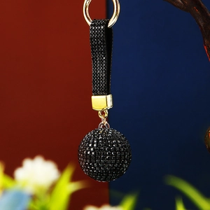 Detail of a luxury black rhinestone ball keychain with a matching strap and gold-tone metal