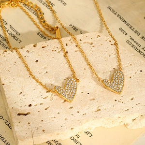 Detailed shot of gold plated heart necklaces with micro pavé crystals on beige stone