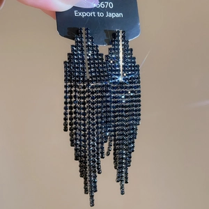 Détail macro de boucles d'oreilles géométriques à pompons noirs et strass scintillants