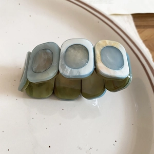 Detail of square resin marble stretch bracelet modules resting on a white ceramic plate