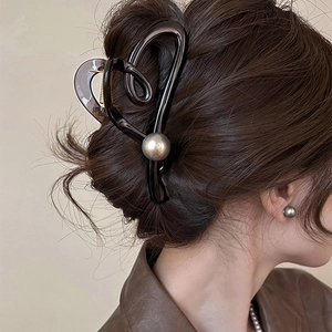 Détail d'une pince à cheveux marron foncé en forme de cœur avec une grande perle