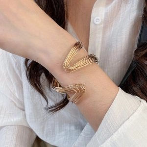 Close-up of a layered gold twisted open bangle worn over a white shirt sleeve