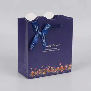 Navy blue paper gift bag with silk ribbon bow and elegant floral patterns on white background
