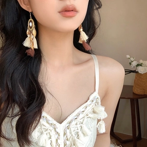 Bohemian style gold leaf earrings with beige and brown tassels worn by a model
