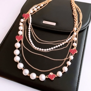 Macro detail of multi-layered gold necklace with white pearls and red heart pendants