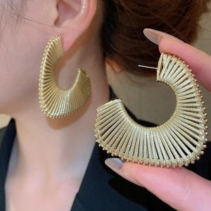 Detailed close-up of golden fan-shaped earrings with textured stripes on model and hand