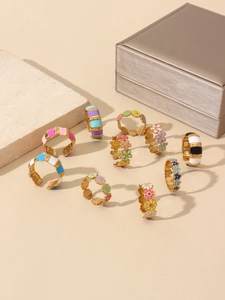 Detail of colorful enamel floral and striped 18k gold plated rings on a stone display