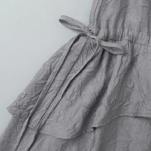 Vue détaillée du tissu plissé gris avec nœud décoratif latéral et ourlet à plusieurs couches