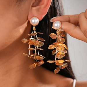 Detailed view of long gold multi-layer leaf earrings with white pearls on a model