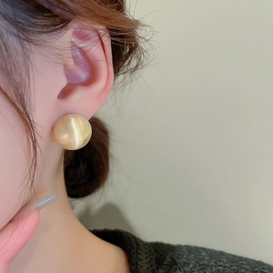 Close-up of golden hemispherical earring with matte brushed texture on model