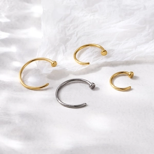 Set of titanium C-shape nose rings in gold and silver colors on a white textured background