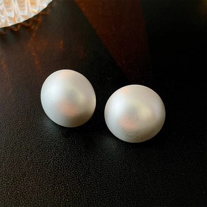 Close-up of minimalist matte white dome stud earrings on black textured leather background