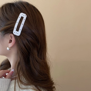 Detail of a white rectangle hair clip with black polka dots on a model with pearl jewelry
