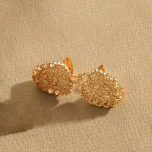 Gros plan de boucles d'oreilles cœur dorées avec surface grainée sur tissu beige