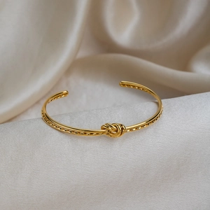 Bracelet jonc ouvert avec nœud plaqué or 18 carats sur un tissu en soie de couleur crème